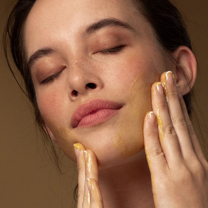 Woman applying Antipodes Grapeseed Butter Cleanser to her face with a neutral background