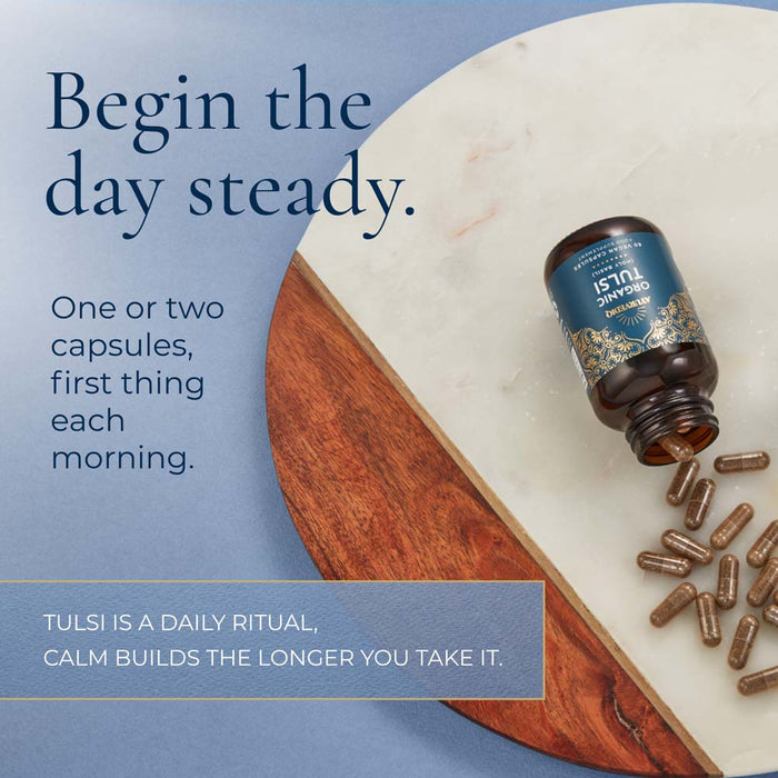 A bottle of Tulsi 15mg Standardized Extract capsules lies on a white marble board with several capsules spilled out onto a blue surface. Large text reads, 'Begin the day steady.'