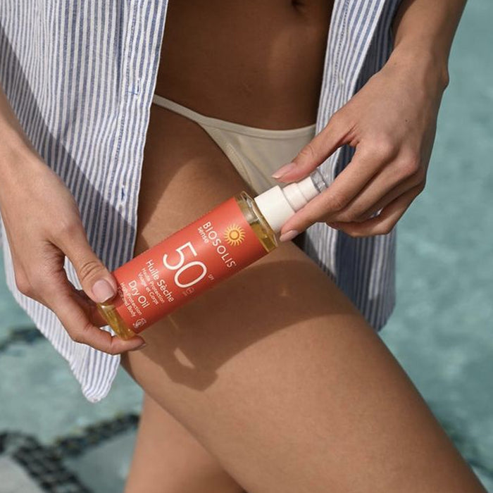 Person applying sunscreen with a bottle labeled 'BioSolis' by a pool.