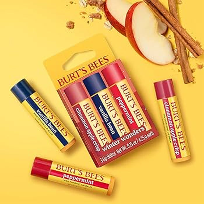 Burt's Bees lip balm packaging on a yellow background with apples and cinnamon sticks.