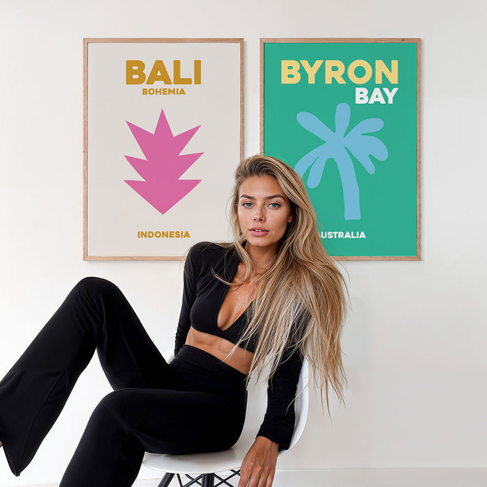 Woman sitting on a chair in front of two framed typography posters, one with 'Bali' and the other with 'Byron Bay'.