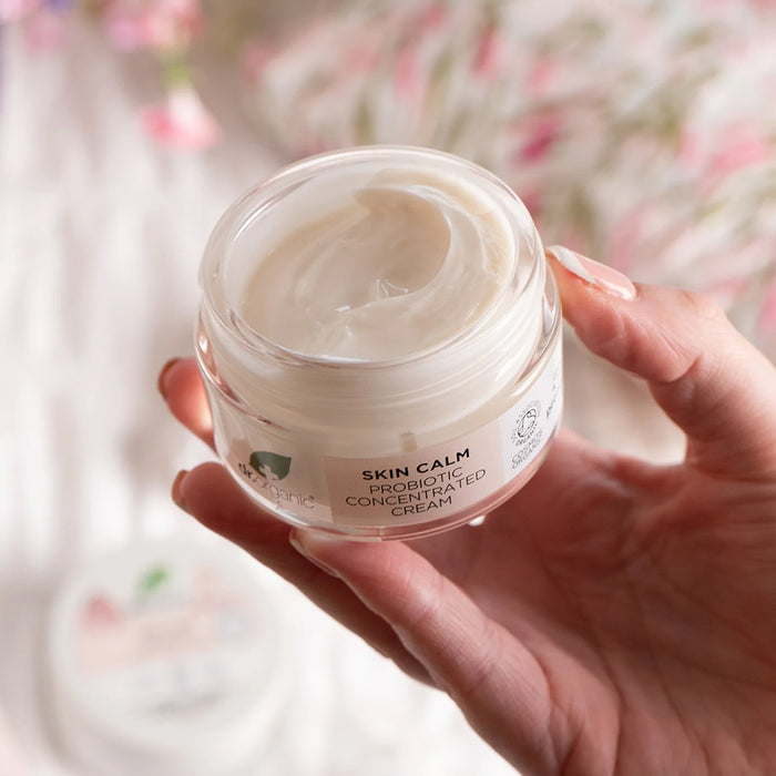 Hand holding a jar of Dr. Organic Skin Calm Probiotic Concentrated Cream with a blurred floral background
