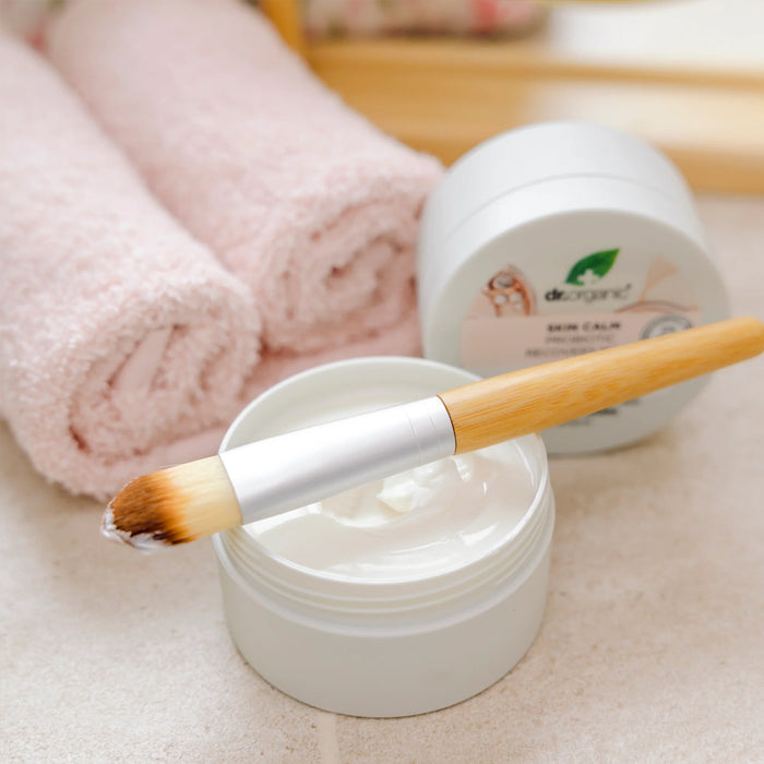 Cosmetic jar with a brush, towel, and container labeled 'Dr. Organic' on a light surface.