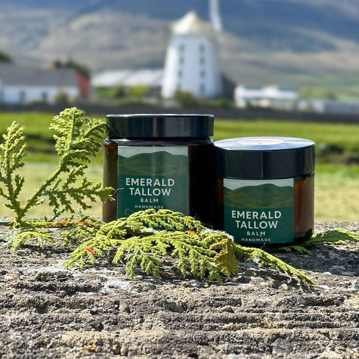 Two jars of Emerald Tallow Balm on a stone surface with a scenic background.