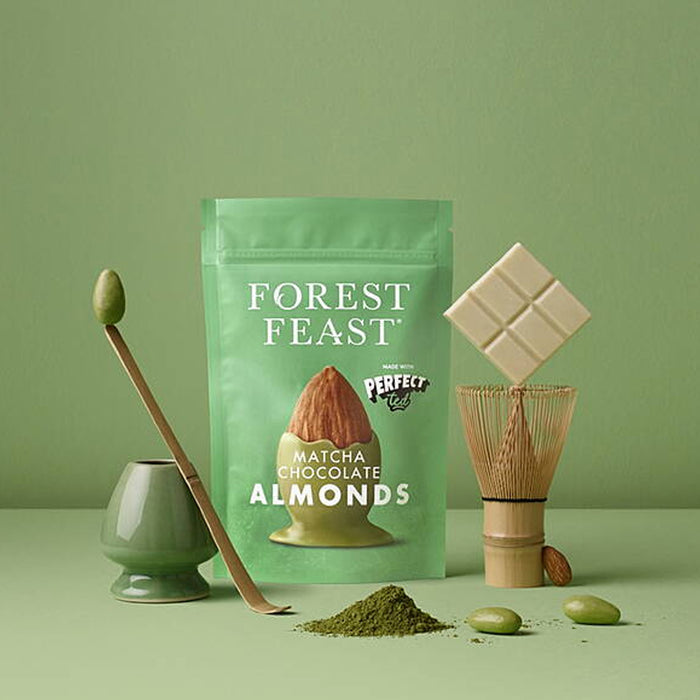 Green package of 'Forest Feast' Matcha Chocolate Almonds with matcha powder and tools on a green background