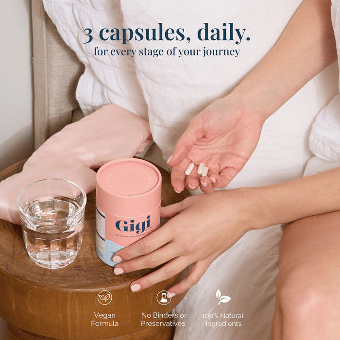 Person holding a pink container labeled 'Gigi' with a glass of water on a wooden table.