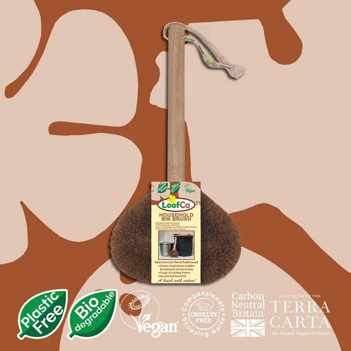 A LooCo hand-washed brown coconut coir brush with a light wood handle and a white drawstring, shown with its product tag against a beige and brown abstract background. Certification badges for 'Plastic Free', 'Bio degradable', 'Vegan', and 'Carbon Neutral Britain' are displayed at the bottom.