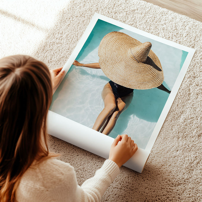 Person unrolling a large photography art print of a person wearing a straw hat showcasing a luxury lifestyle.