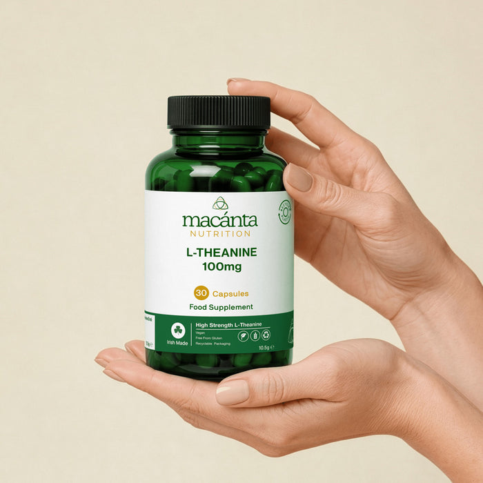 A person's hands holding a green bottle of Macanta Nutrition L-Theanine 100mg food supplement capsules against a beige background.