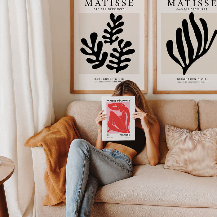 Girl sitting on a couch holding a Matisse poster in front of her face, with two Matisse framed prints on the wall.