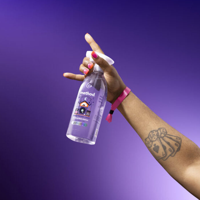 Hand holding a Method cleaning spray bottle against a purple background