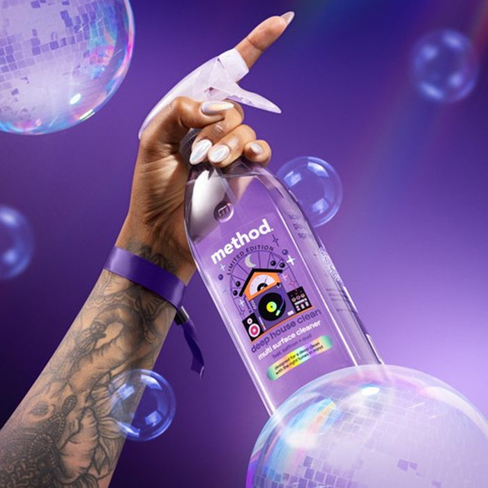 Hand holding a Method cleaning spray bottle with bubbles in the foreground on a purple background