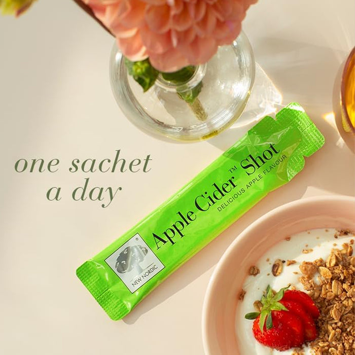 Green apple cider shot package with a bowl of yogurt and granola on a light surface.