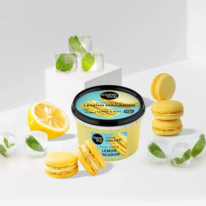 Organic Shop Lemon Macaron Firming Body Scrub surrounded by lemons, macarons, and ice cubes on a light background.
