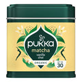 A tin of Pukka Matcha Vanilla Chai organic tea, featuring a dark green metal container with a pale yellow label decorated with green leaves, white flowers, and black silhouettes.