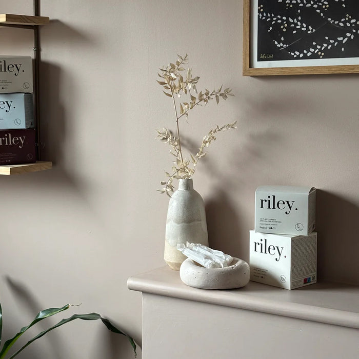 Decorative items on a shelf with 'riley.' products against a neutral wall.
