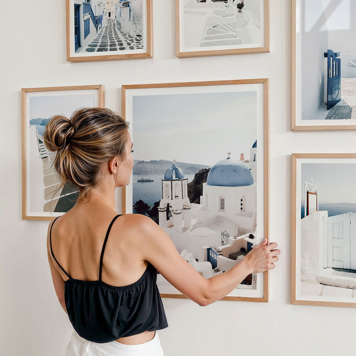 Woman arranging framed art prints on a wall. They are all photography print from Europe, Santorini in Greece.