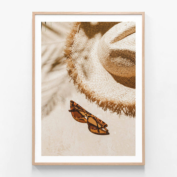 A framed photo wall art print featuring a sun hat and sun glasses on the beach on a sunny day