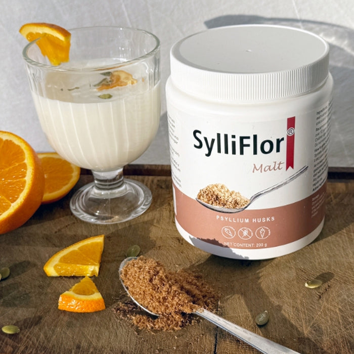 A white plastic jar of SylliFlour Malt , shown next to a glass of milk with orange slices on a wooden surface.