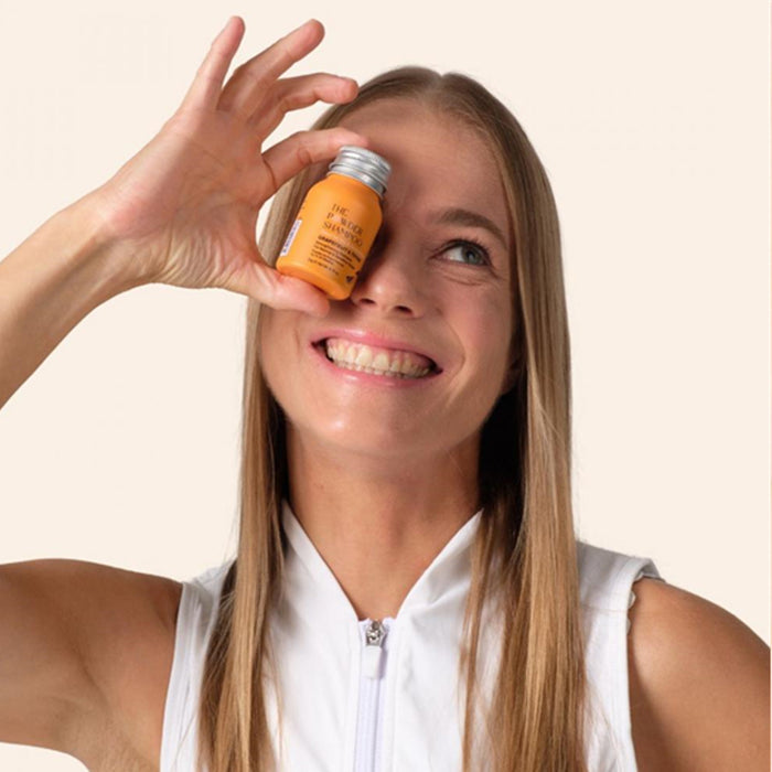 Woman holding a small jar to her eye against a plain background