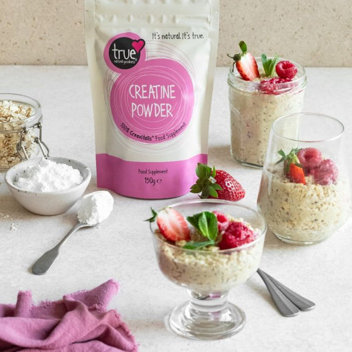 Bag of true Creatine Powder with glasses of a dessert topped with strawberries and raspberries on a white surface.