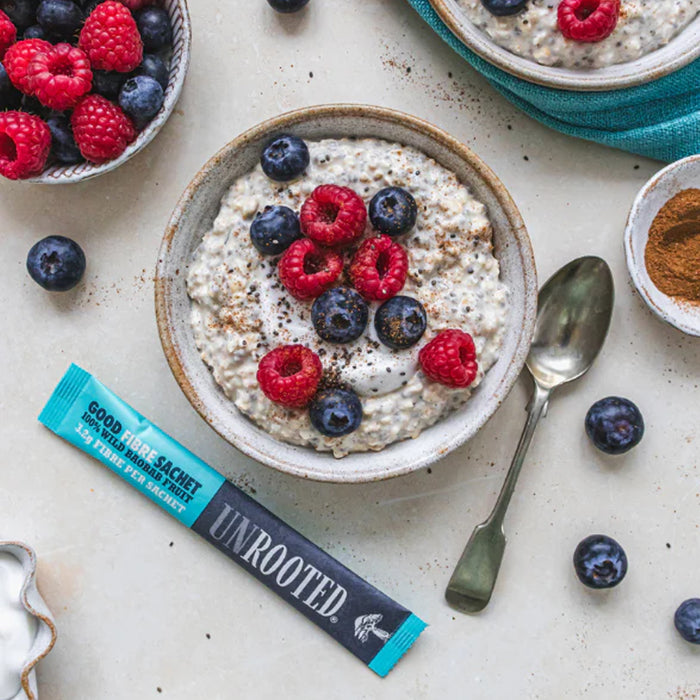 Bowl of oatmeal with berries and a Unrooted product on a light surface