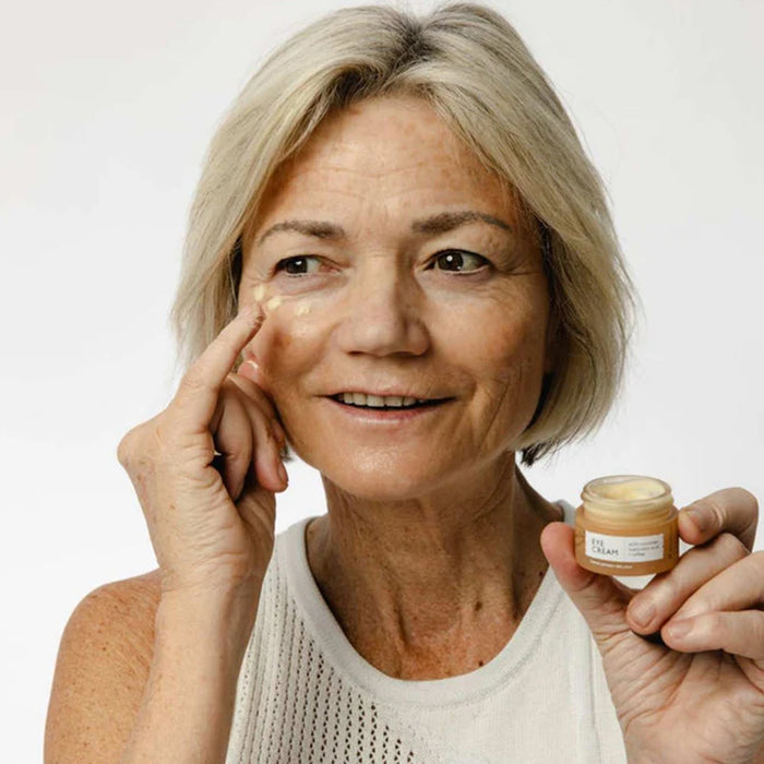 Woman applying UpCircle Eye Cream to her face with a jar of cream in her hand on a white background