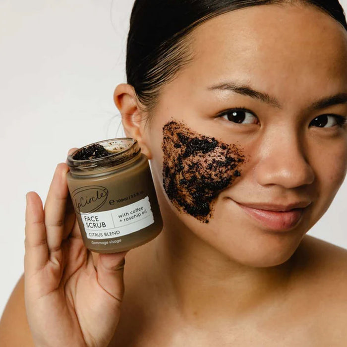 Woman applying coffee face scrub with a jar of the product.