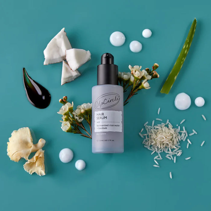 Hair serum bottle surrounded by natural ingredients on a teal background