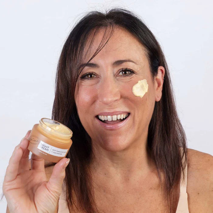 Woman applying cream to her face with a jar of Upcircle Night Cream cream.