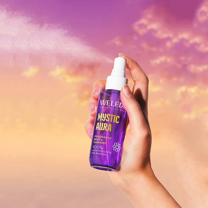 A hand holding a purple spray bottle with mist spraying from the nozzle.